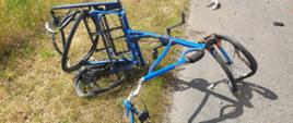 Zdjęcie przedstawia całkowicie zniszczony rower 3-kołowy, przeznaczony dla osoby niepełnosprawnej znajdujący się na poboczu drogi. 