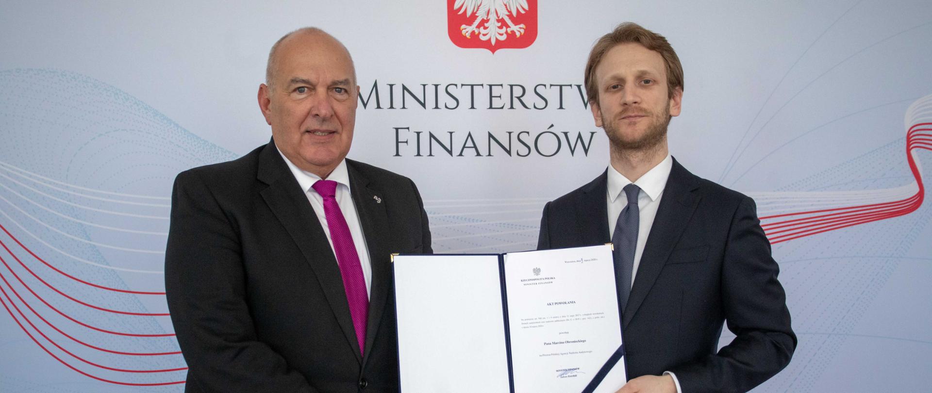 Minister Tadeusz Kościński i prezes PANA Marcin Obraniecki na tle baneru Ministerstwa Finansów