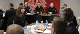 Warsztatowa część narady szkoleniowej dyżurnych stanowisk kierowania PSP województwa opolskiego. Strażacy w umundurowaniu służbowym i dowódczo-sztabowym na sali sztabowej w KW PSP w Opolu. W tle kierownictwo wydziału operacyjnego KW PSP w Opolu oraz st. bryg. Arkadiusz Kuśmierski Zastępca Opolskiego Komendanta Wojewódzkiego PSP w Opolu.