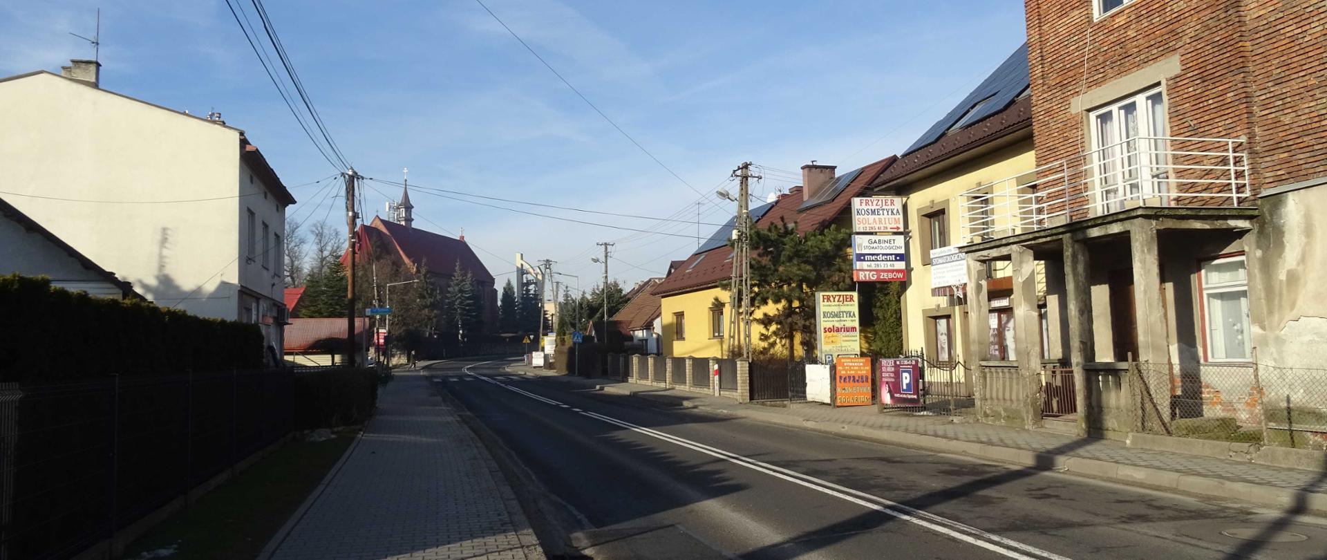 droga przechodząca przez centrum miejscowości, wzdłuż drogi domy, w tle kościół