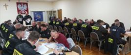 Na zdjęciu widać druhów OSP siedzących przy stołach w trakcie pisania egzaminu teoretycznego. Zdjęcie wykonane na świetlicy Komendy Powiatowej PSP w Oleśnie.