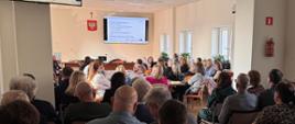 W sali przy stołach siedzi grupa osób i słucha wykładu o Krajowym Systemie e-Faktur