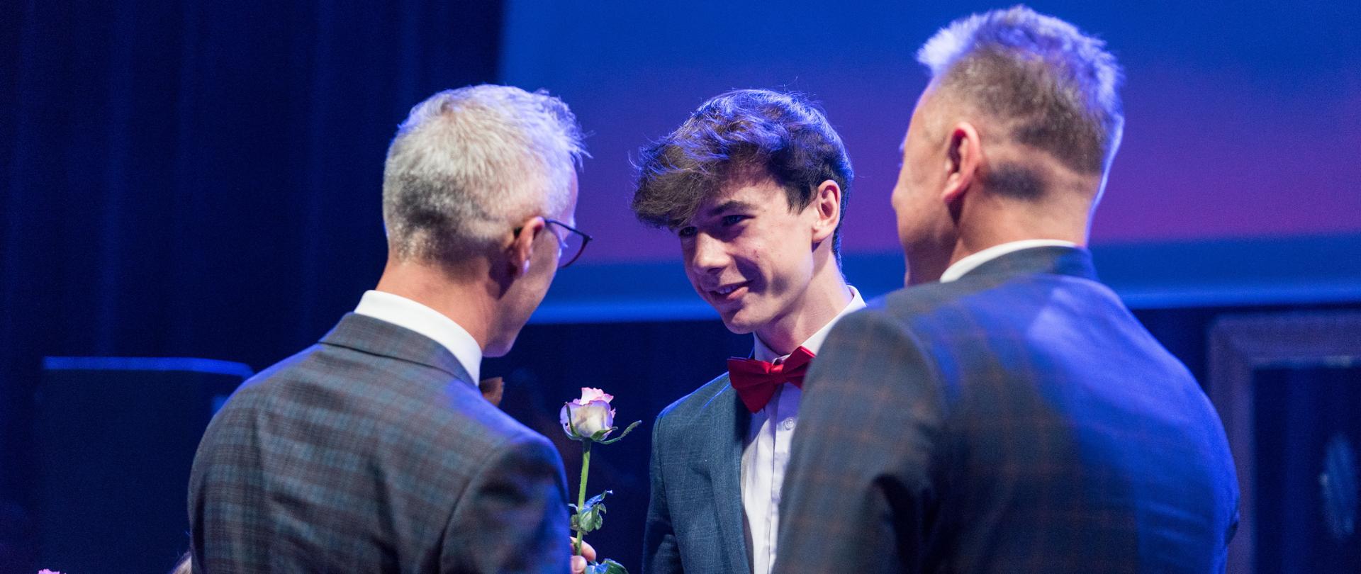 Laureat stoi na scenie i odbiera nagrodę.