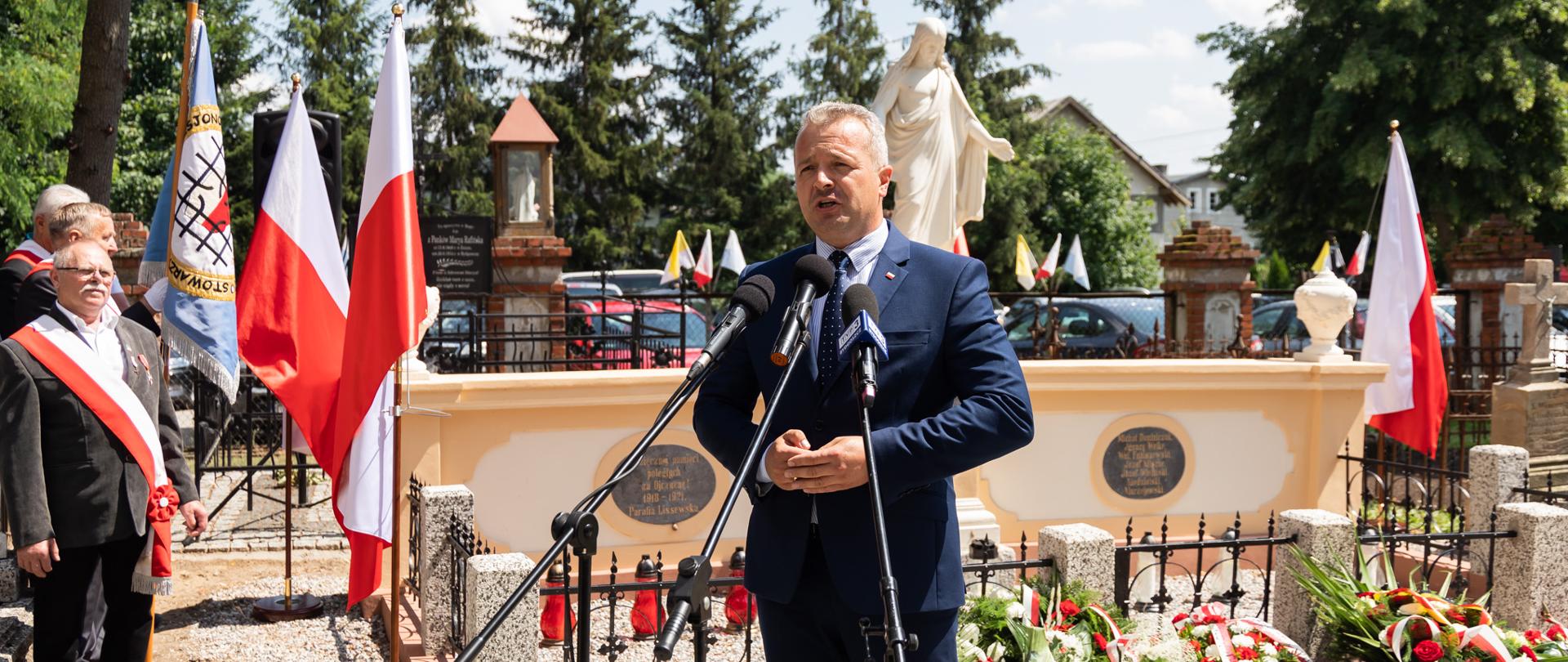 Mężczyzna stojący przed mikrofonami na cmentarzu