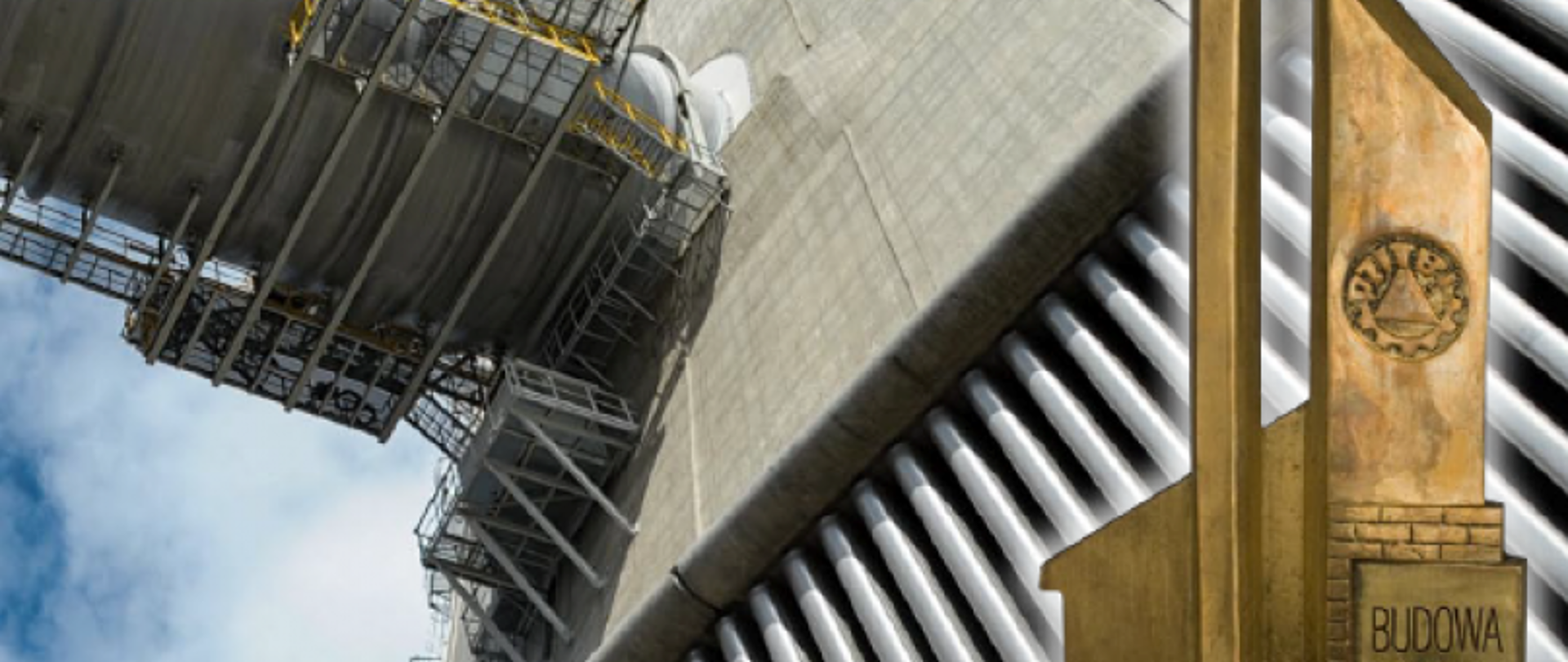 Przemysłowa konstrukcja z rusztowaniami i rurami, z przodu pomnik z napisem „BUDOWA” i emblematem „PIŁA”.