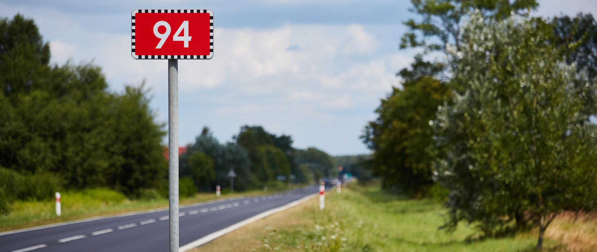 Droga krajowa o numerze 94, widoczny znak z numerem drogi w oddali droga i zielone pobocze, brak chodnika