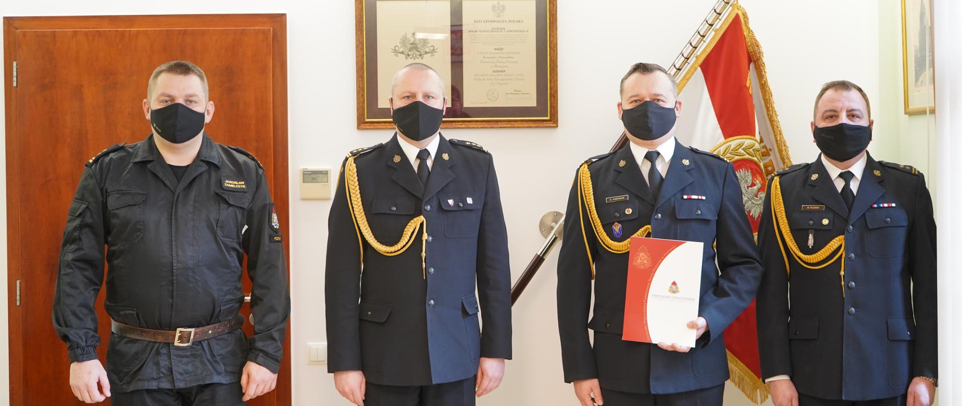zdjęcie grupowe czterech strażaków stojacych w maseczkach, w tle sztandar 