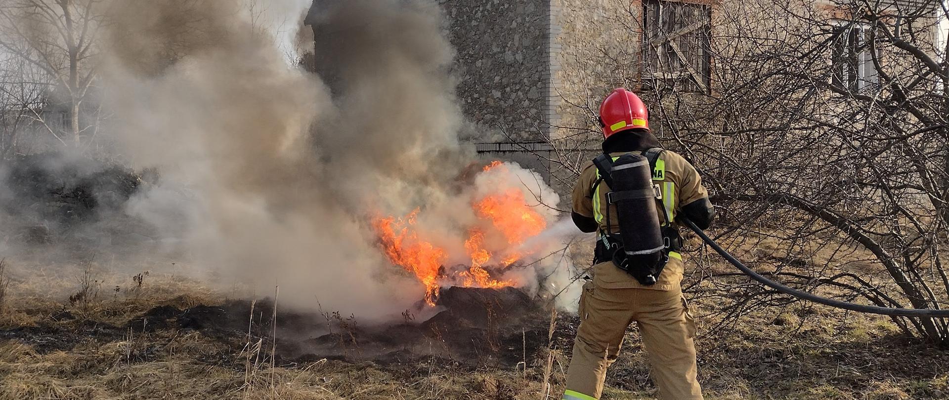 Strażak gaszący pożar opon na terenie posesji przed budynkiem 