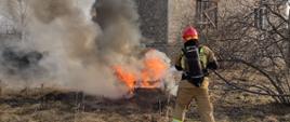 Strażak gaszący pożar opon na terenie posesji przed budynkiem 