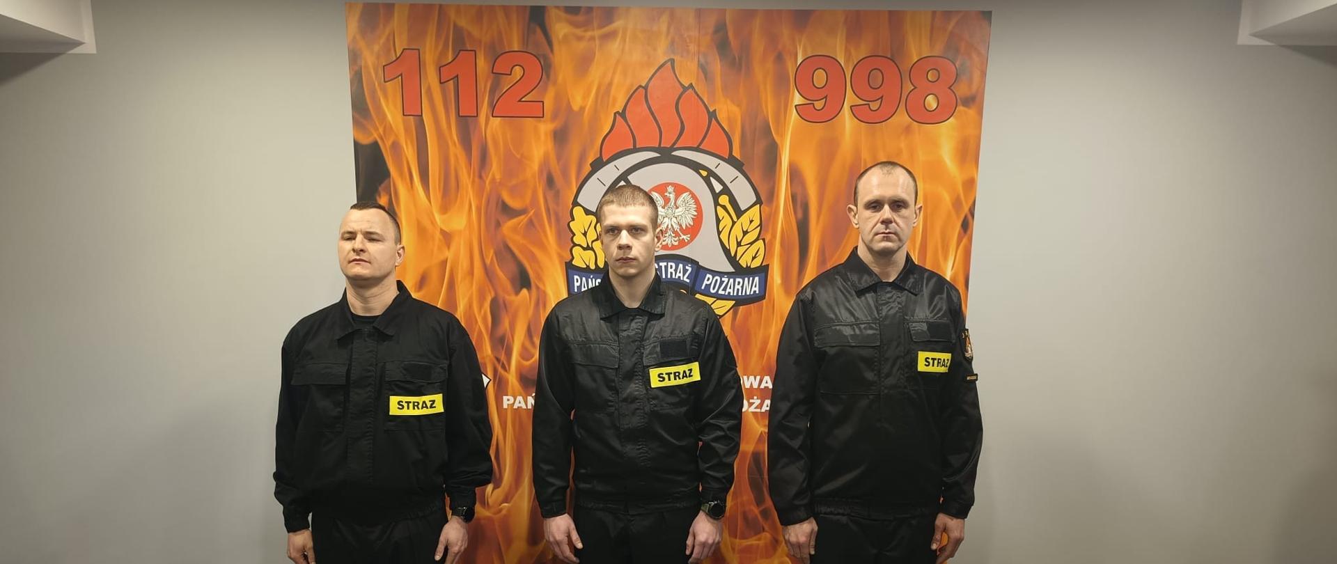 Na zdjęciu trzech młodych strażaków przed ślubowaniem. Stoją obok siebie na świetlicy.