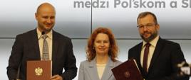 Minister funduszy i polityki regionalnej Grzegorz Puda stoi i trzyma w dłoniach dokument porozumienia o współpracy w obszarze polityki spójności między Polską a Słowacją, po jego lewej stronie stoi wicepremier Republiki Słowacji ds. planu odbudowy i funduszy europejskich Lívia Vašákova oraz minister inwestycji, rozwoju regionalnego i informatyzacji Republiki Słowackiej Peter Balík
