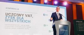 Premier Mateusz Morawiecki stoi przy mównicy na tle napisu: Konferencja uczciwy VAT, zysk dla wszystkich.
