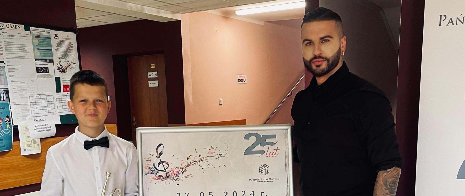 Zdjęcie ucznia Franciszka Brzózki oraz nauczyciela Wojciecha Szeli obok banera reklamowego konkursu