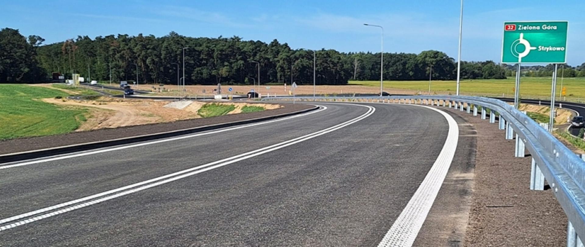 Nowa droga z oznaczeniami i znakiem kierunkowym do Zielonej Góry i Strykowa, otoczona zielenią i lasem.