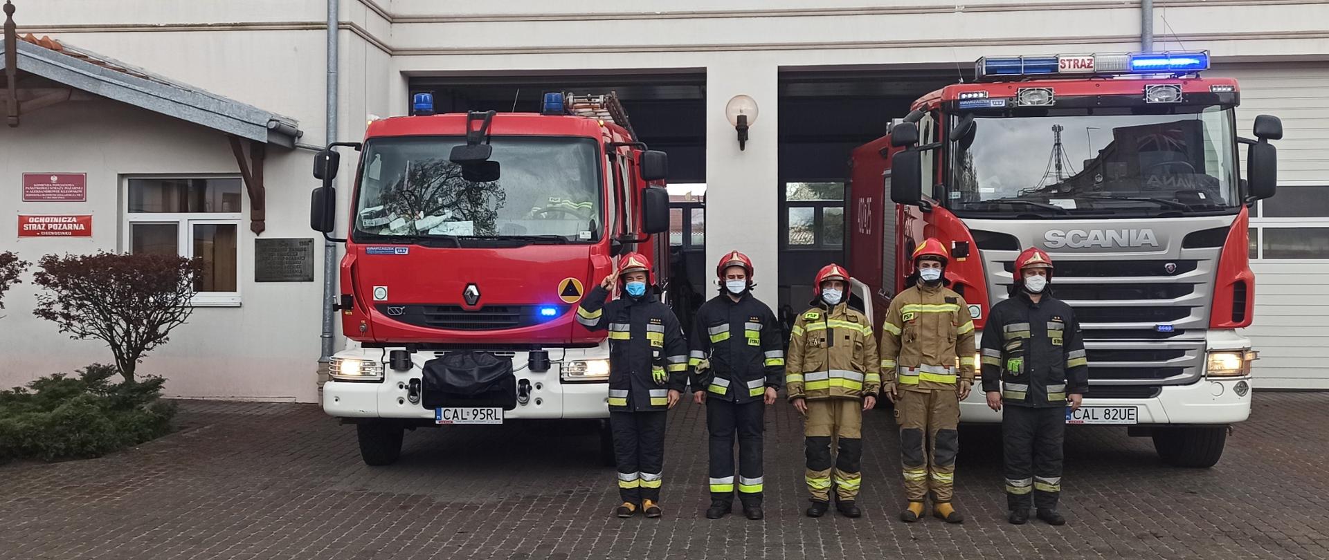 Na pierwszym planie widocznych pięciu strażaków w umundurowaniu specjalnym. Oddają honory ku pamięci solidaryzując się z zastrzelonym na służbie policjantem. Stoją na tle samochód pożarniczych. w tle widoczny budynek JRG w Ciechocinku