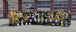 Zdjęcie przedstawia kilkudziesięciu strażaków OSP którzy ukończyli szkolenie podstawowe. Ubrani są w umundurowanie specjalne a w rękach trzymają zaświadczenia o ukończeniu szkolenia.