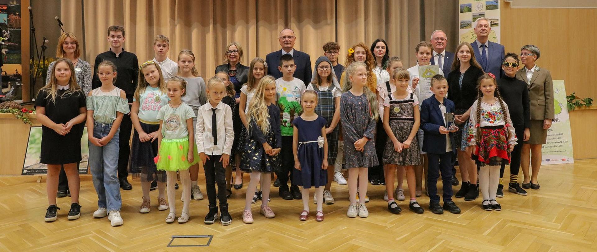 W dużej sali do zdjęcia pozuje grupa kilkudziesięciu osób, dorosłych i dzieci. W tle na ekranie znajduje się napis Lubuskie Ekologiczne.