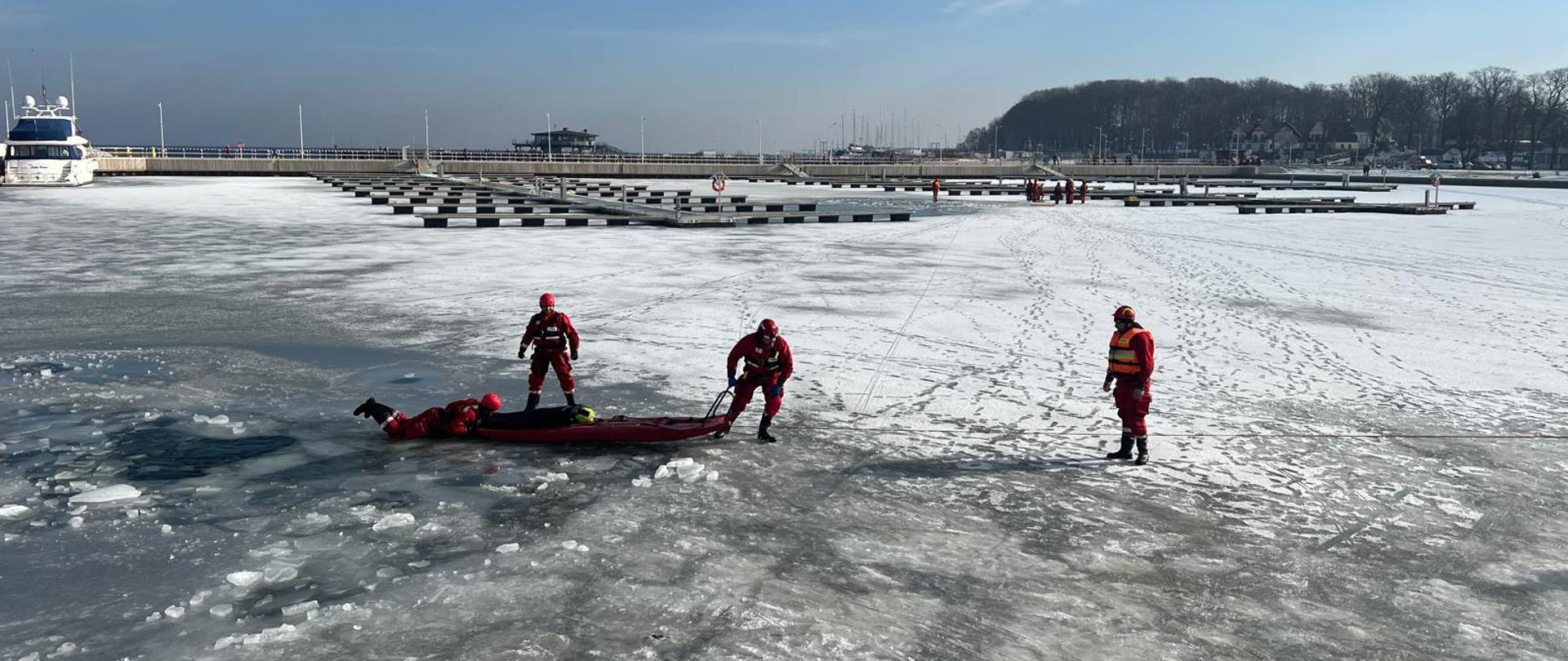 Ratownicy podejmują manekina z wody. W tle widać Marinę oraz molo w Pucku