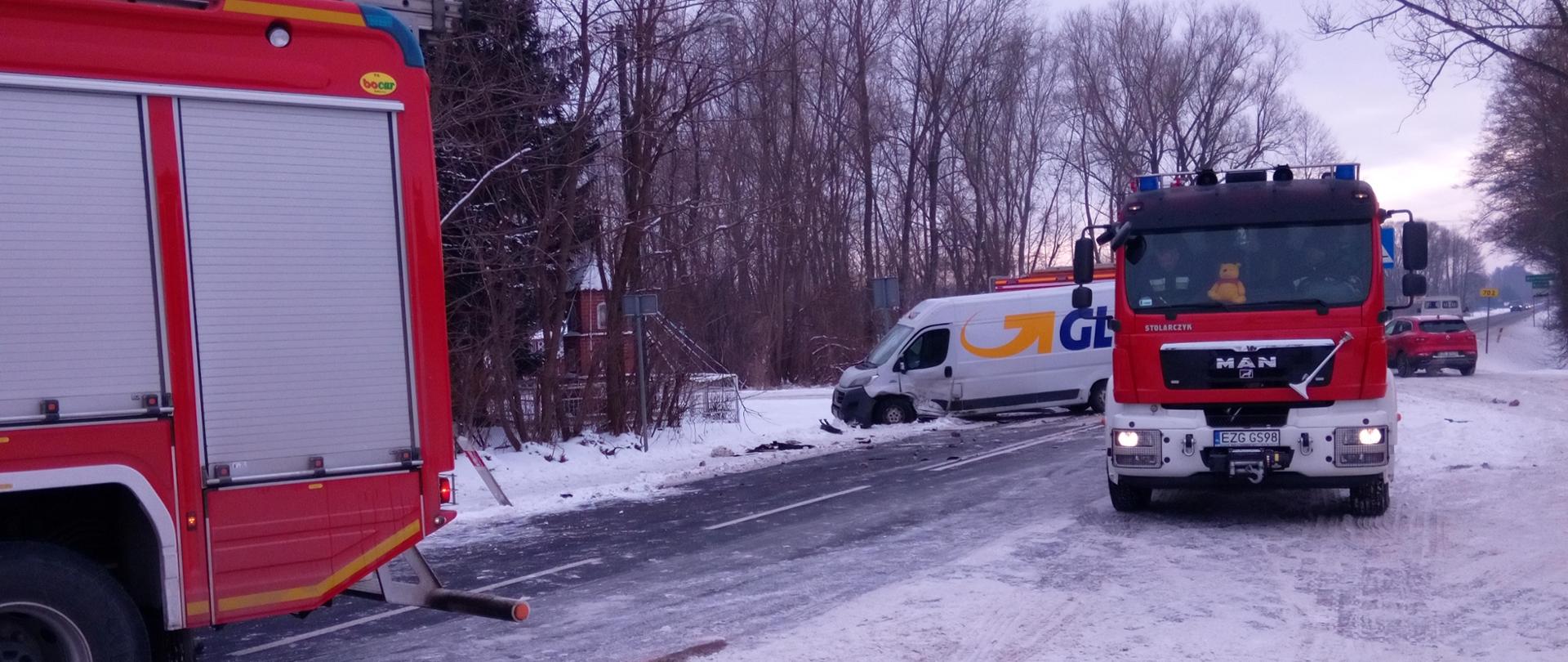 Na zdjęciu na pierwszym planie widać dwa samochody ratowniczo gaśnicze które, zabezpieczają miejsce kolizji. Natomiast na drugim planie widać samochód dostawczy który, brał udział w kolizji.