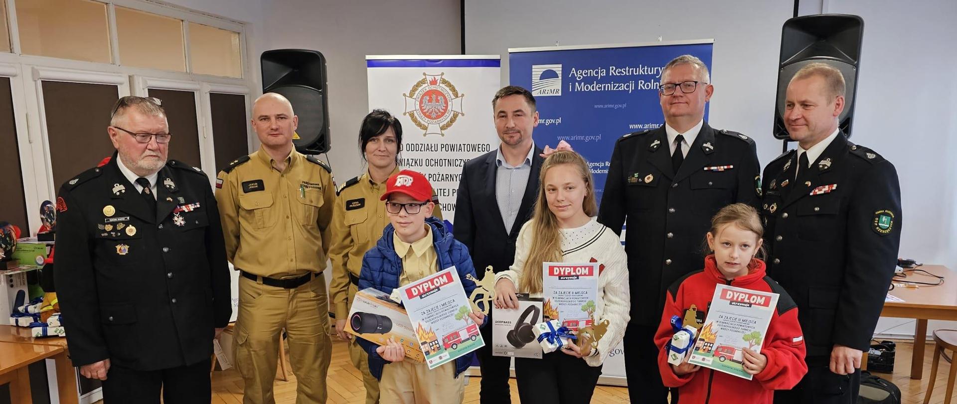 Zdjęcie grupowe komisji sędziowskiej podczas wręczania nagród laureatom eliminacji powiatowych. Laureaci trzymają dyplomy oraz otrzymane nagrody.