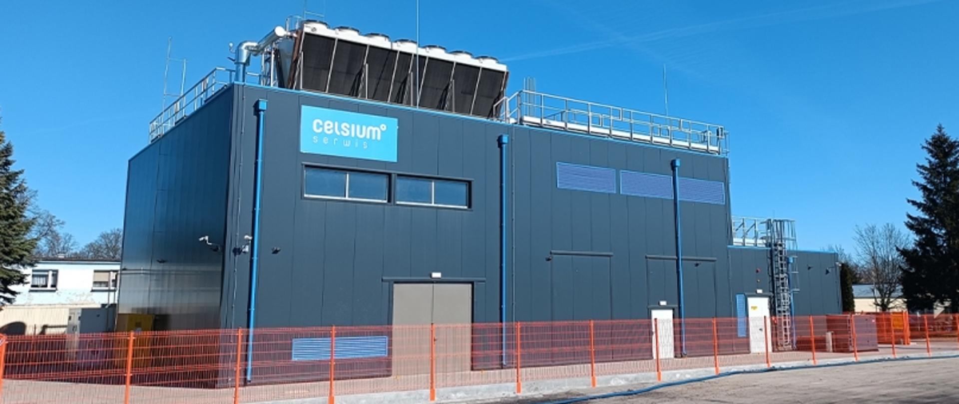 Szary budynek, który znajduje się za metalowym ogrodzeniem.