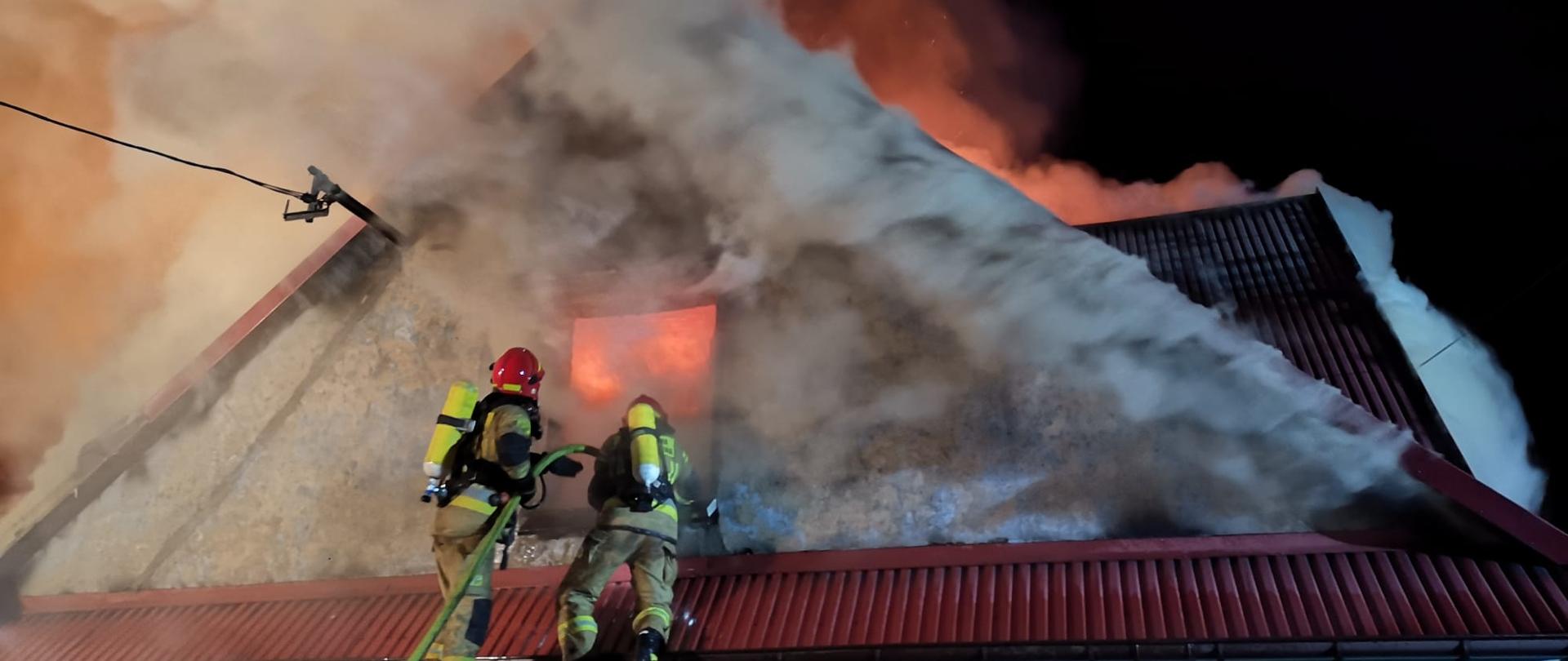 Zdjęcie przedstawia płonący budynek oraz strażasów
