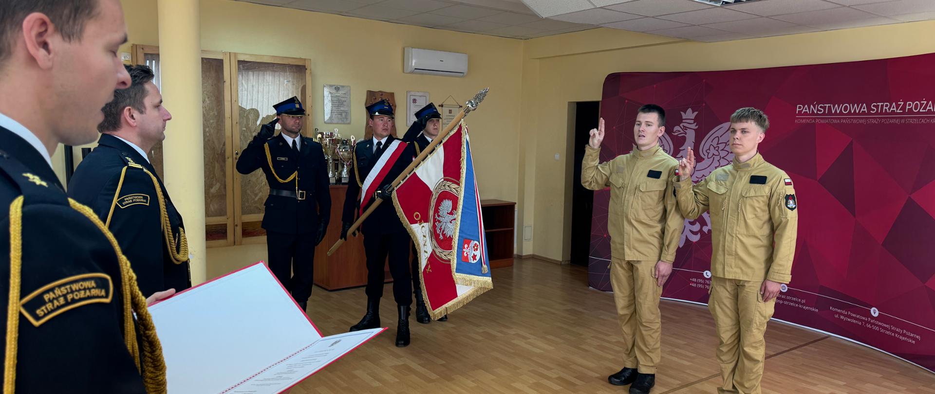 Zdjęcie przedstawia moment składania przysięgi przez nowych strażaków. Na dalszym planie znajduje się poczet sztandarowy.