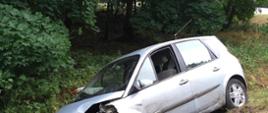 Zdjęcie przedstawia rozbity samochód osobowy marki Renault Scenic znajdujący się w przydrożnym rowie. 