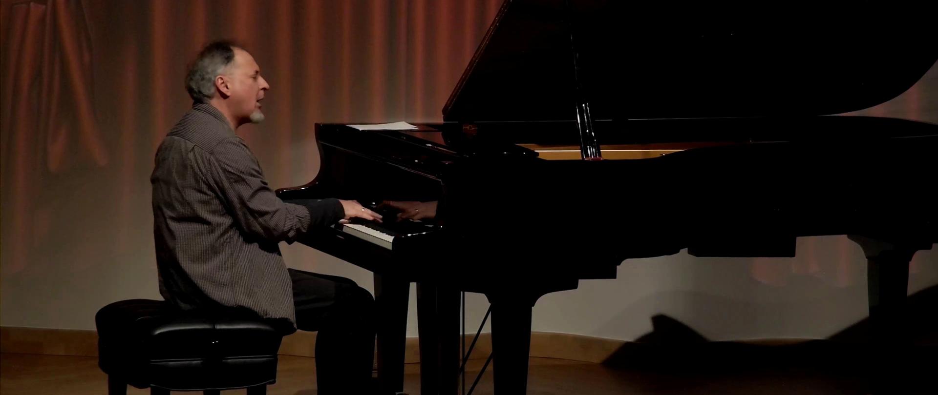 Zdjęcie. Na estradzie sali koncertowej pianista gra na dużym czarnym fortepianie.