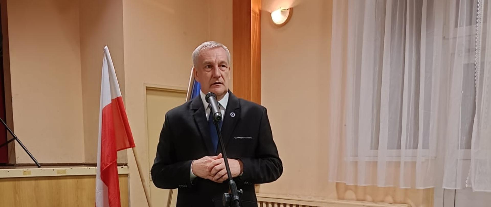 Osoba cywilna przemawia stojąc przy mikrofonie na sali.