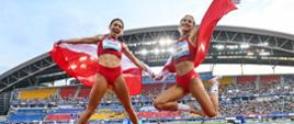 Dwie kobiety w czerwonych sportowych ubraniach skaczą i machają polskimi flagami na środku wielkiego stadionu.