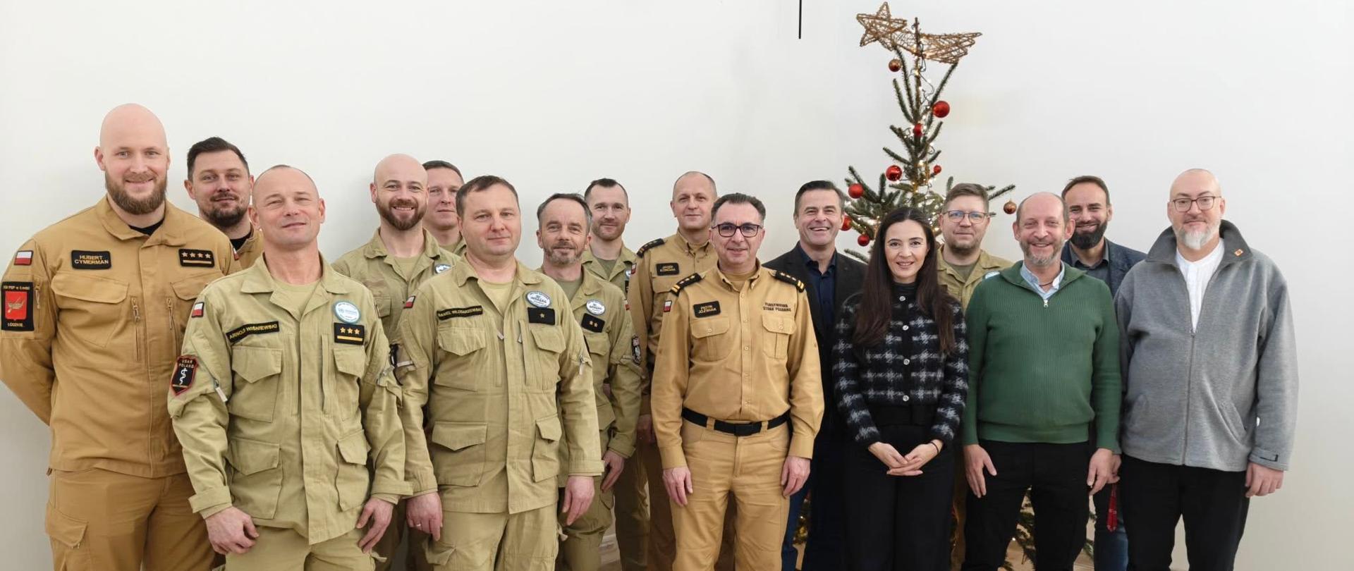 Na zdjęciu na tle choinki w sali konferencyjnej strażacy, kierownictwo km psp w łodzi oraz przedstawiciele domu wschodniego