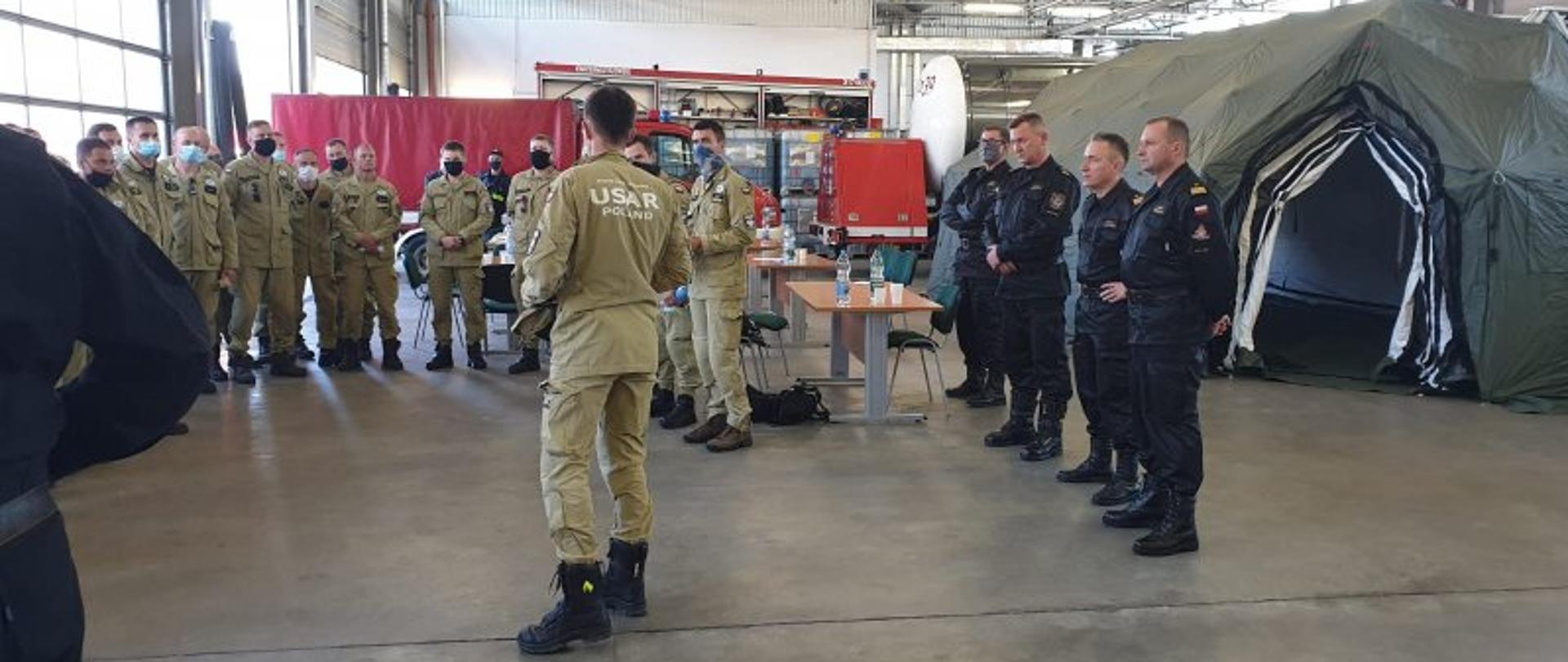 POLSCY STRAŻACY Z MISJĄ RATOWNICZĄ W BEJRUCIE – na zdjęciu duża hala, rozstawiony namiot, i dwie grupy strażaków. Wśród nich nadbryg. Andrzej Bartkowiak komendanta główny PSP. 