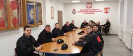 Na zdjęciu strażacy z Ochotniczych Straży Pożarnych przed egzaminem kończącym szkolenie naczelników OSP. Strażacy ubrani w ubrania koszarowe koloru czarnego bez czapek na sali wykładowej siedzą na krzesłach przed owalnym stole w Komendzie Powiatowej Państwowej Straży Pożarnej w Gorlicach.