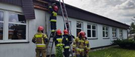Strażacy rozbierają elementy budynku szkoły. Działania prowadzą z wykorzystaniem drabin.