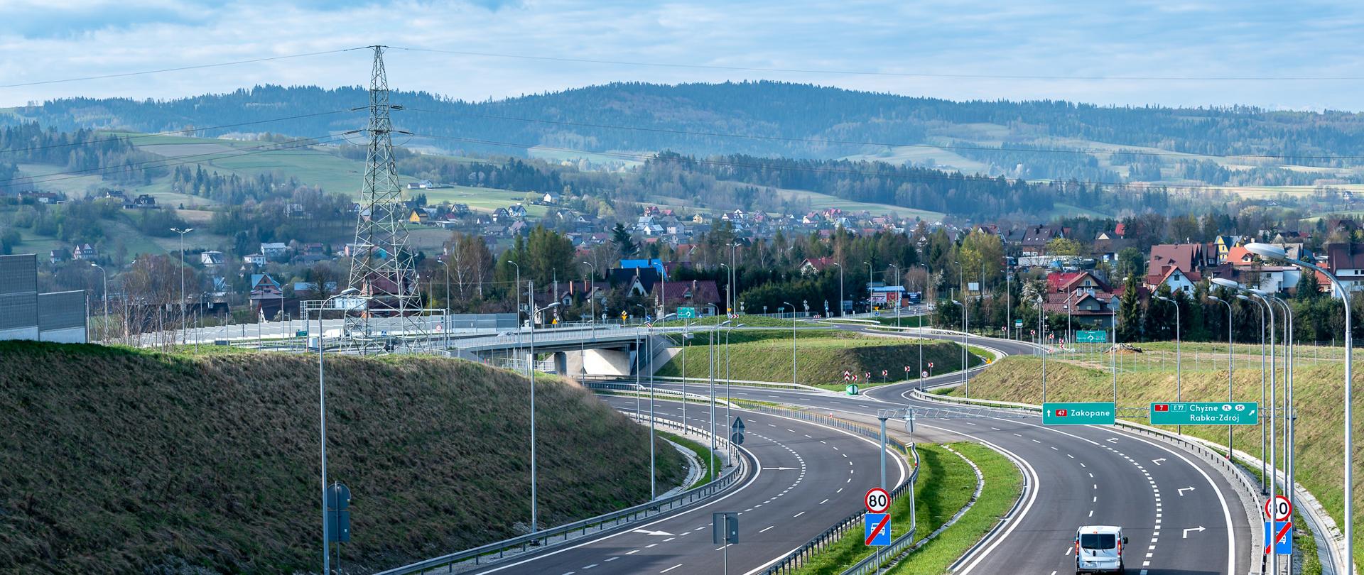 Droga dwujezdniowa i węzeł drogowy w górskim terenie, w tle zabudowania i pasmo górskie