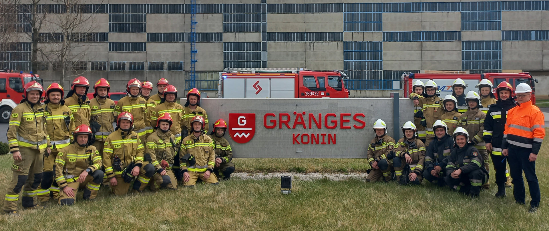 Zdjęcie przedstawia strażaków oraz samochody strażackie przed banerem firmy GRANGES Konin po zakończonych ćwiczeniach. 