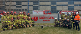 Zdjęcie przedstawia strażaków oraz samochody strażackie przed banerem firmy GRANGES Konin po zakończonych ćwiczeniach. 