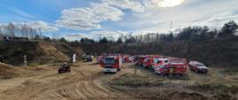 Pojazdy pożarnicze ustawione jeden obok drugiego w półokręgu na terenie kopalni (w dole). Oczekiwanie na rozpoczęcie szkolenia