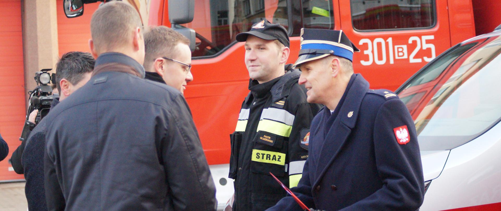 Zdjęcie przedstawia dwóch funkcjonariuszy Państwowej Straży Pożarnej podczas uroczystego odebrania aktu przekazania samochodu 