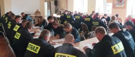 Na zdjęciu widać druhów OSP siedzących przy stołach w trakcie pisania egzaminu teoretycznego.
Zdjęcie wykonane na świetlicy Komendy Powiatowej PSP w Oleśnie. W tle widać naczelnika wydziału ośrodka szkolenia KW PSP w Opolu - st. bryg. Wiesława Eliasza.