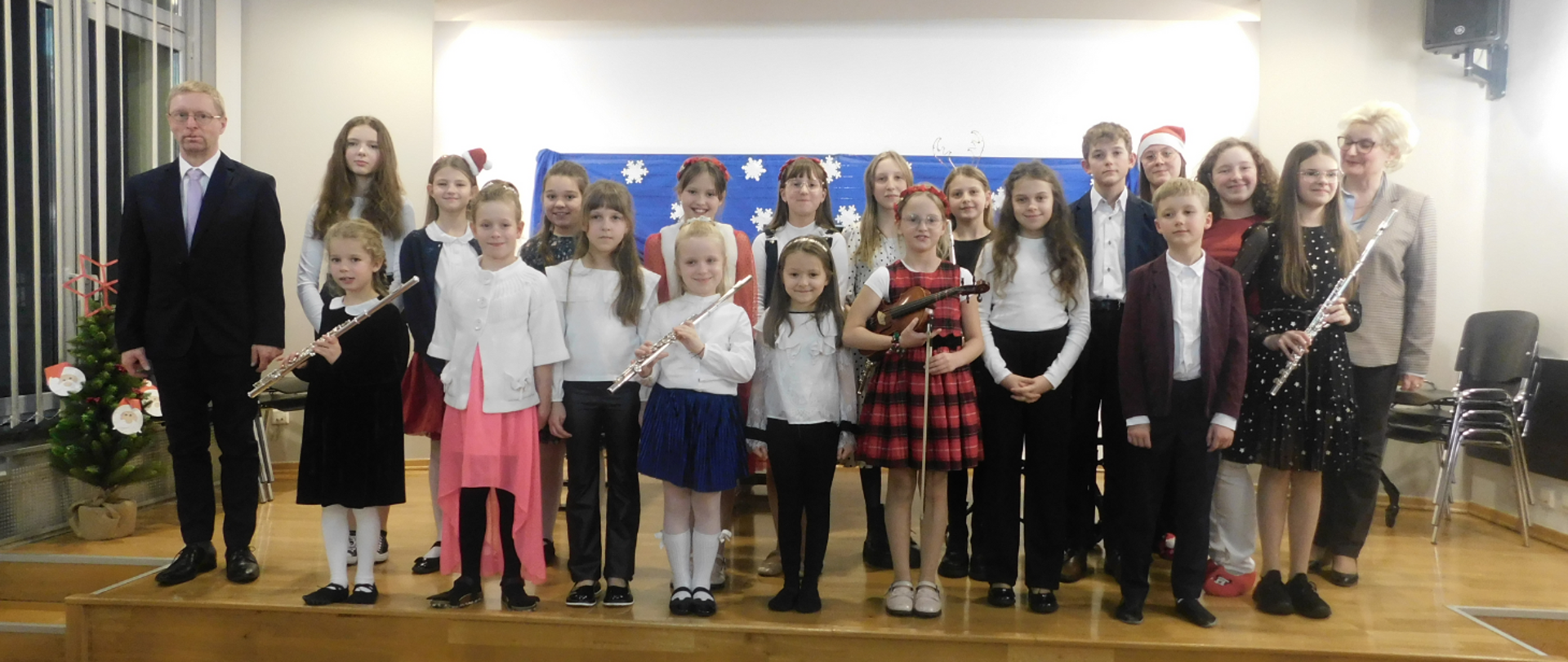 Na zdjęciu grupa uczniów, którzy wystąpili podczas koncertu. Niektórzy z nich trzymają instrument: flet poprzeczny i skrzypce.