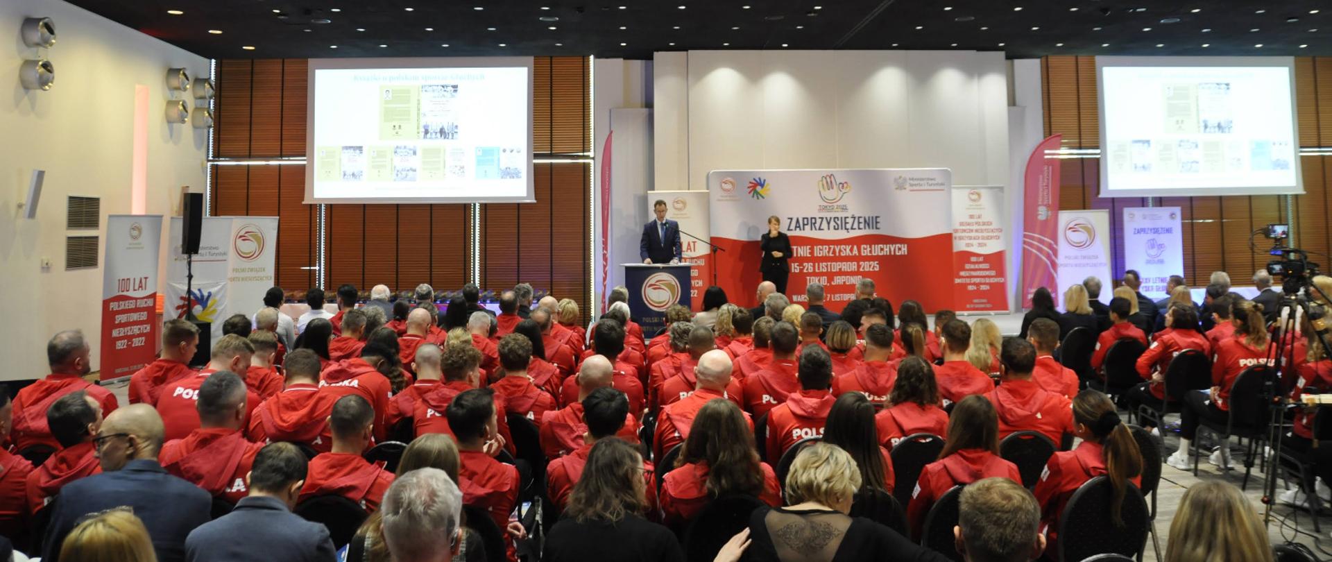 Zaprzysiężenie reprezentacji Polski na XXV Letnie Igrzyska Głuchych - Tokio 2025. Na zdjęciu widać salę pełną siedzących ludzi i scenę.