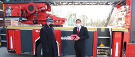 Na tle samochodu pożarniczego z drabiną mechaniczną po prawej stronie stoi Dyrektor Generalny Rosenbauer Karlsruhe Pana Michael Kristeller trzymając w rękach wycięty z blachy symboliczny kluczyk do samochodu i przekazuje go stojącemu po jego prawej stronie Kujawsko-Pomorskiemu Komendantowi Wojewódzkiemu Państwowej Straży Pożarnej starszemu brygadierowi Jackowi Kaczmarkowi.