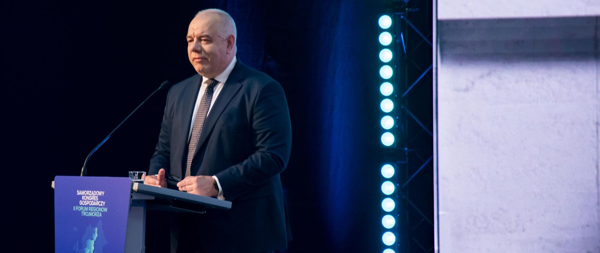 Wicepremier Jacek Sasin przy mównicy, ujęcie z boku.