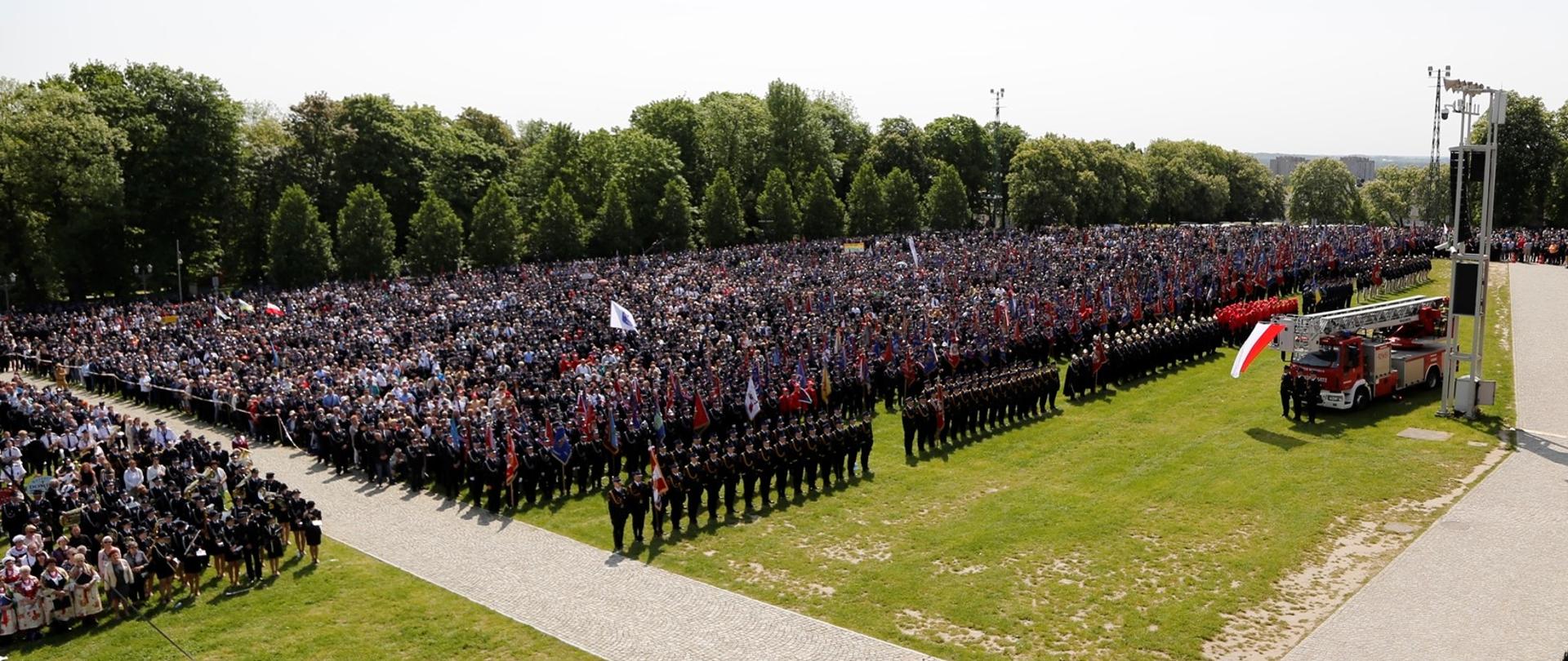 Widok z góry na pielgrzymów zebranych na błoniach jasnogórskich po prawej samochód bojowy drabina z biało-czerwoną flagą przymocowaną na szczycie drabiny