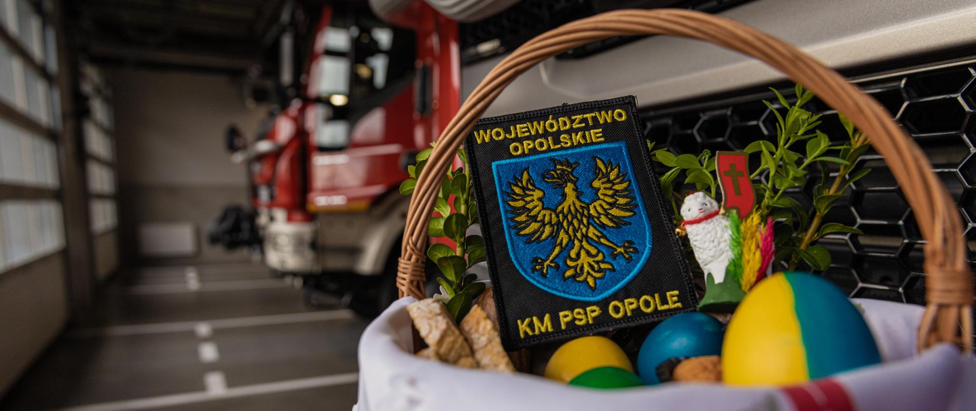 Koszyk wielkanocny na tle samochodu strażackiego. W koszyku naszywka z napisem "województwo opolskie" oraz "KM PSP OPOLE"
