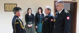 Fotografia przedstawia uroczysty apel na świetlicy komendy powiatowej Państwowej Straży Pożarnej w Mielcu zorganizowany z okazji pożegnania w związku z zakończeniem pełnienia służby przez dwóch funkcjonariuszy: st.bryg. Witolda Strzępkę – dowódcy jednostki ratowniczo-gaśniczej oraz ogn. Marka Grzelaka –ratownika-kierowcę.
Na zdjęciu odchodzący na emeryturę funkcjonariusze zdają obowiązki służbowe a meldunek odbiera zastępca podkarpackiego komendanta wojewódzkiego st.bryg. Andrzej Marczenia. Strażacy ubrani w umundurowanie galowe koloru granatowego. Na drugim planie stoją bliscy strażaków. 