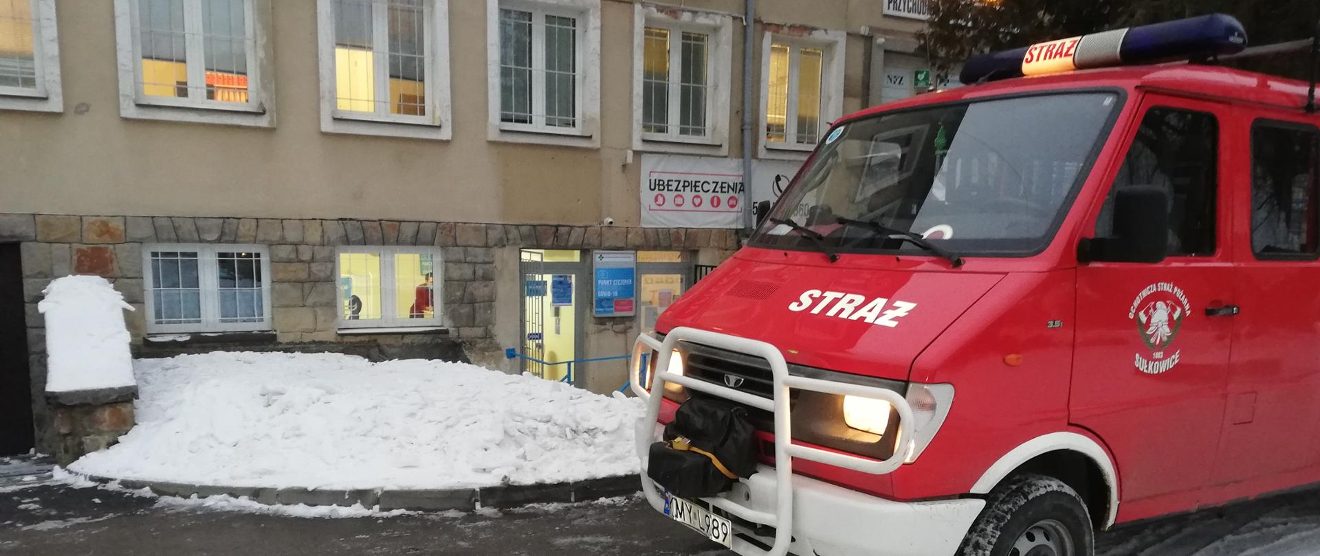 Na zdjęciu widoczne otwarte drzwi do punktu szczepień przeciw Covid-19 oraz samochód OSP Sułkowice przed budynkiem, którym realizowane są przewozy osób na szczepienia.