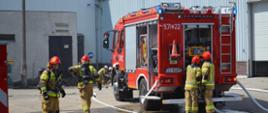 Zdjęcie przedstawia samochód gaśniczy z liniami wężowymi oraz strażaków PSP w trakcie ćwiczeń na terenie zakładu "Purmo" w Wałczu na ul. Budowlanych 10